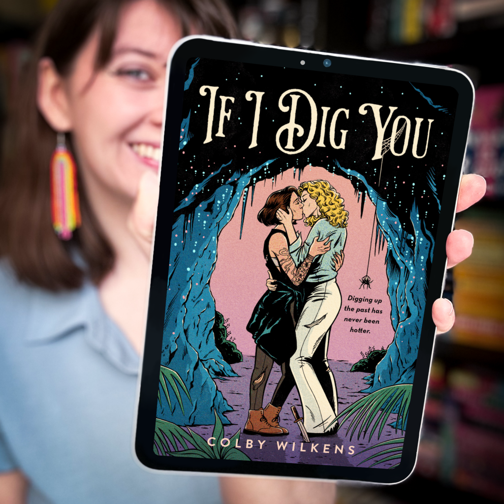 woman in blue shirt and rainbow earrings holding up iPad with cover of If I Dig You by Colby Wilkens on it.